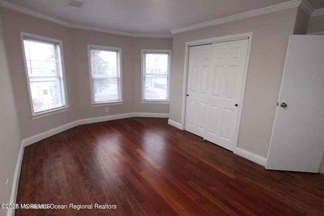unfurnished bedroom featuring dark wood-type flooring, baseboards, crown molding, and a closet