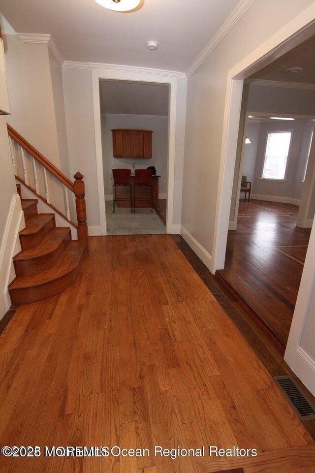 corridor featuring crown molding, wood finished floors, stairway, and baseboards