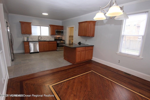 kitchen featuring stainless steel appliances, a sink, dark countertops, a peninsula, and baseboards