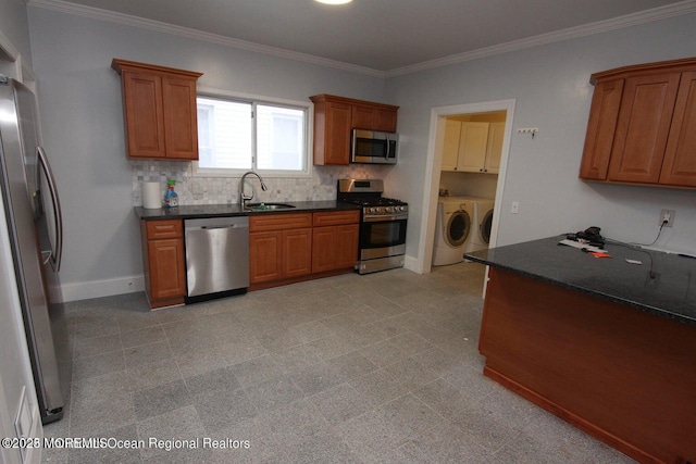 kitchen featuring stainless steel appliances, washer and dryer, a sink, brown cabinets, and decorative backsplash