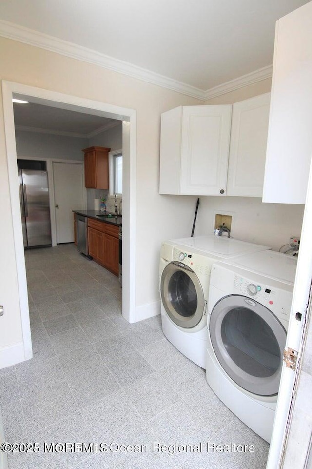 laundry room featuring washing machine and clothes dryer, cabinet space, baseboards, and crown molding