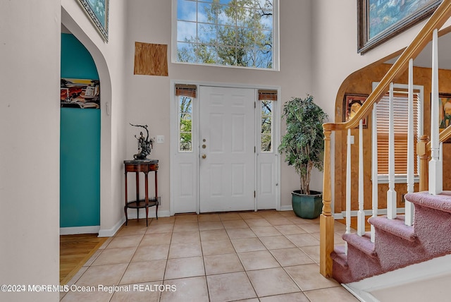 entryway with a high ceiling, stairs, light tile patterned floors, baseboards, and arched walkways