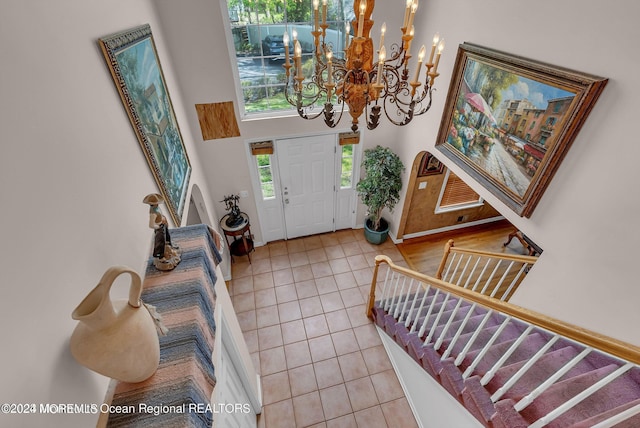 entryway with tile patterned floors, a chandelier, stairway, a towering ceiling, and baseboards
