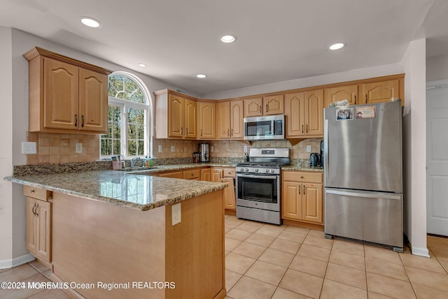 kitchen with appliances with stainless steel finishes, light stone counters, a peninsula, backsplash, and light tile patterned flooring