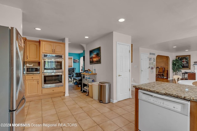 kitchen with stainless steel appliances, arched walkways, recessed lighting, light tile patterned flooring, and light stone counters