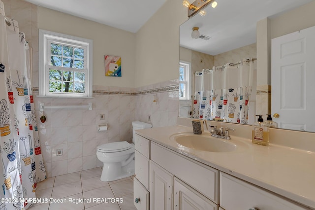full bathroom with tile patterned flooring, tile walls, toilet, vanity, and wainscoting