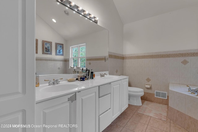 bathroom with tile patterned flooring, tile walls, toilet, wainscoting, and double vanity