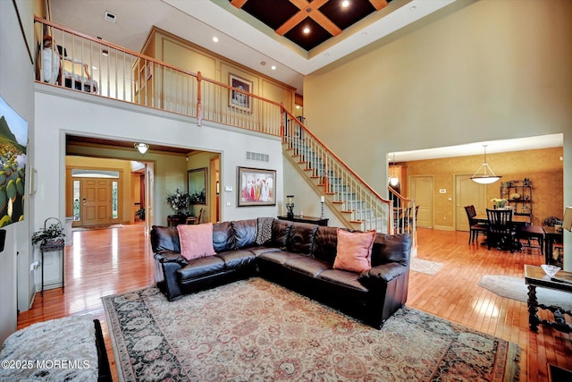 living room featuring a towering ceiling, stairway, wood-type flooring, coffered ceiling, and beam ceiling