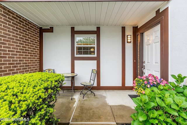 property entrance featuring stucco siding, covered porch, and brick siding