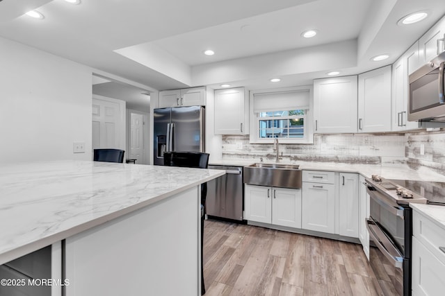 kitchen with appliances with stainless steel finishes, a sink, light stone counters, decorative backsplash, and light wood-style flooring