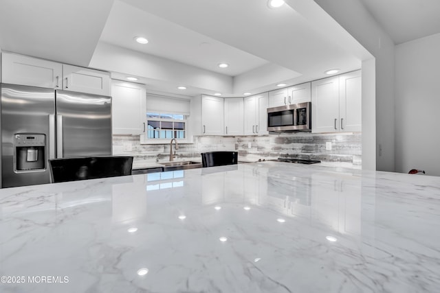 kitchen with stainless steel appliances, a sink, backsplash, light stone counters, and recessed lighting