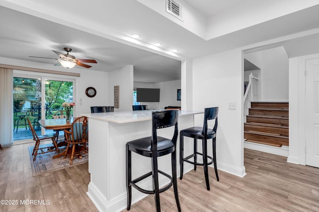 kitchen with light wood-style flooring, ceiling fan, a breakfast bar area, a peninsula, and baseboards