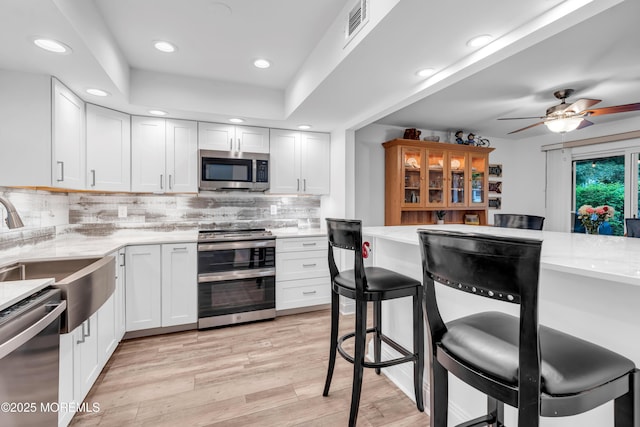 kitchen with stainless steel appliances, a kitchen bar, recessed lighting, light wood finished floors, and tasteful backsplash