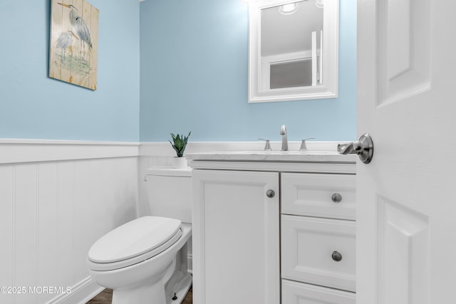 half bathroom with a wainscoted wall, toilet, and vanity