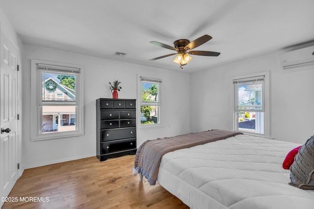 bedroom with a wall mounted AC, light wood-style flooring, ceiling fan, and baseboards