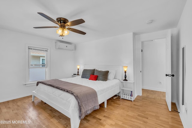 bedroom with a wall mounted air conditioner, light wood-style floors, baseboards, and ceiling fan
