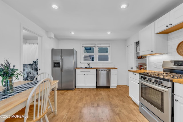 kitchen with appliances with stainless steel finishes, butcher block countertops, tasteful backsplash, white cabinets, and recessed lighting