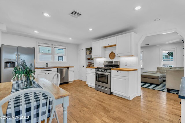 kitchen featuring stainless steel appliances, wooden counters, white cabinets, tasteful backsplash, and recessed lighting