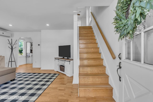 staircase featuring a wall mounted AC, arched walkways, wood finished floors, recessed lighting, and baseboards