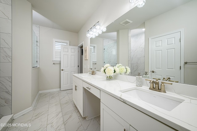 bathroom with marble finish floors, a tile shower, baseboards, and double vanity