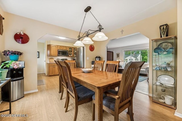 dining area featuring arched walkways, light wood finished floors, and baseboards