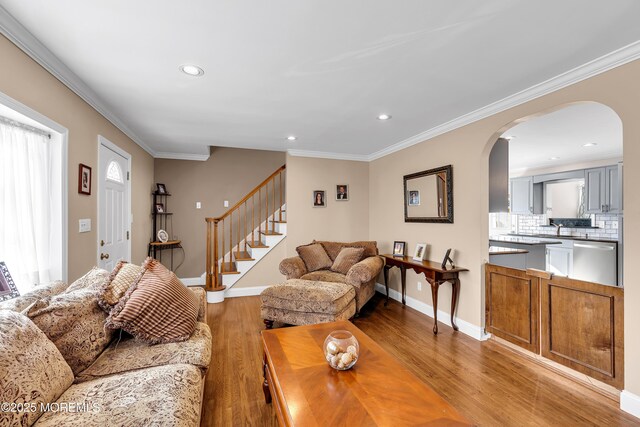 living area featuring light wood finished floors, arched walkways, stairway, recessed lighting, and crown molding