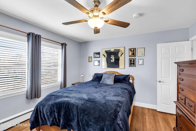 bedroom featuring a baseboard heating unit, wood finished floors, baseboards, and a ceiling fan