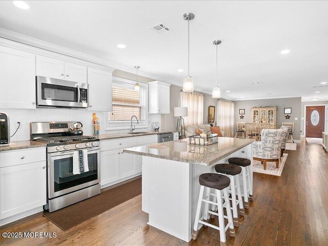 kitchen with appliances with stainless steel finishes, open floor plan, white cabinets, crown molding, and a breakfast bar area