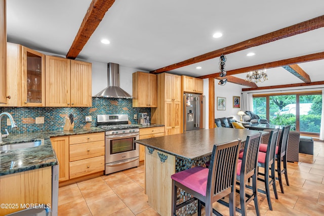 kitchen featuring appliances with stainless steel finishes, wall chimney range hood, a sink, beam ceiling, and dark countertops