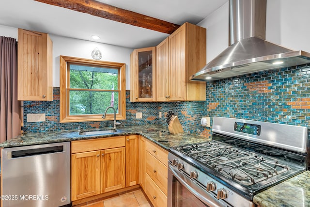 kitchen with appliances with stainless steel finishes, wall chimney exhaust hood, a sink, dark stone countertops, and glass insert cabinets