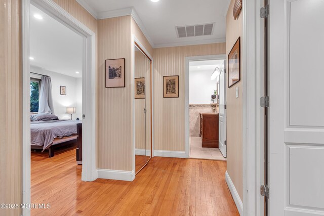 hallway with light wood-style floors, ornamental molding, and baseboards