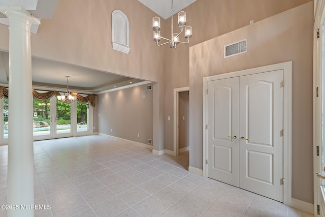 unfurnished living room featuring a chandelier, light tile patterned floors, a high ceiling, baseboards, and decorative columns