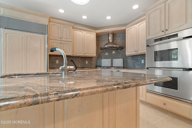 kitchen with double oven, wall chimney range hood, paneled fridge, a sink, and decorative backsplash