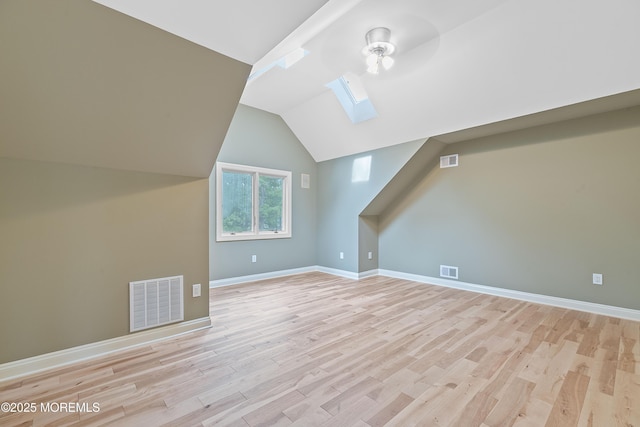 additional living space featuring a skylight, light wood-style flooring, baseboards, and vaulted ceiling