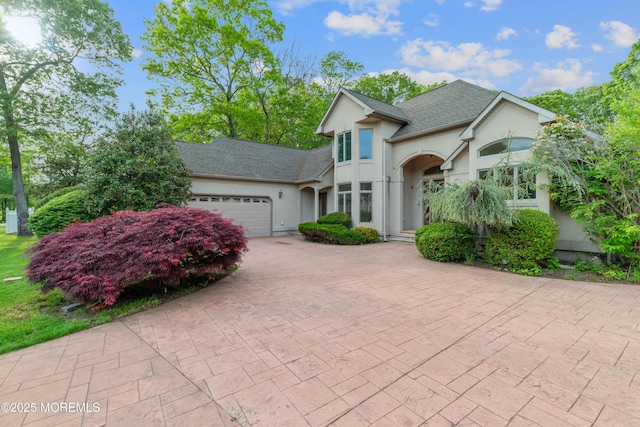 view of front of property featuring stucco siding, an attached garage, decorative driveway, and roof with shingles