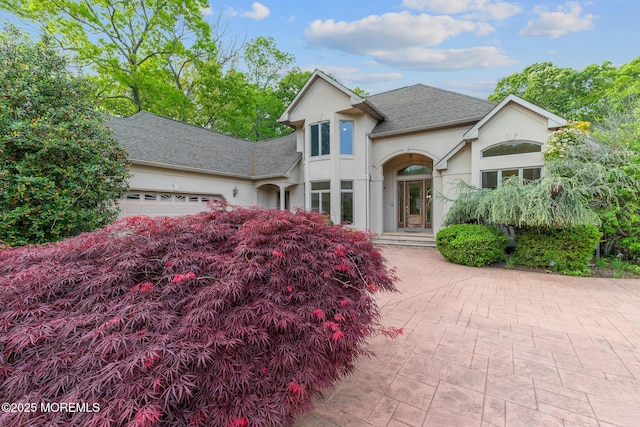 view of front of house featuring an attached garage, roof with shingles, stucco siding, and driveway