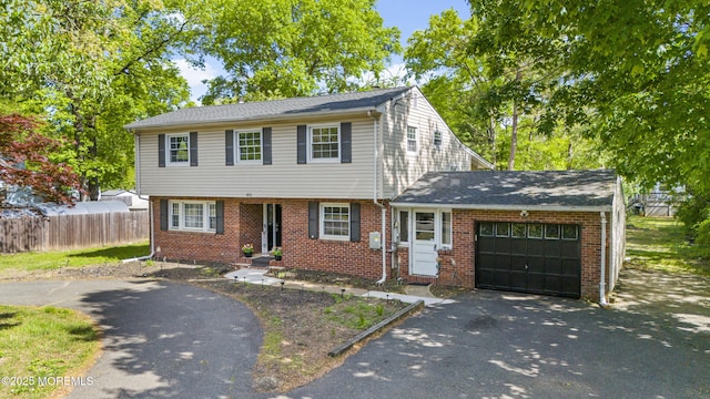 colonial house featuring driveway, an attached garage, fence, and brick siding