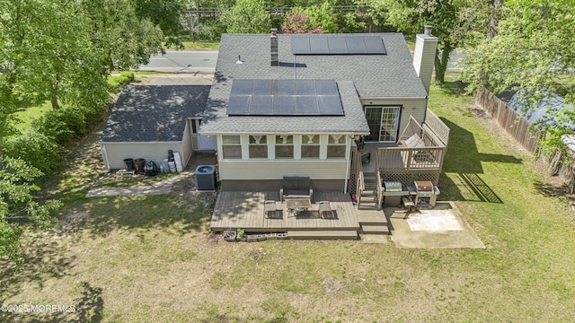 rear view of property featuring a chimney, a wooden deck, central air condition unit, roof with shingles, and solar panels