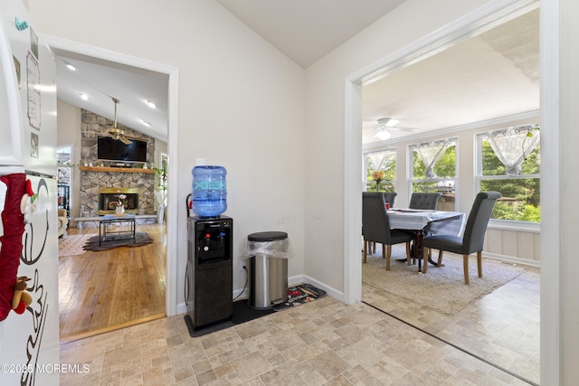 office area featuring lofted ceiling, ceiling fan, baseboards, light stone finish flooring, and a stone fireplace
