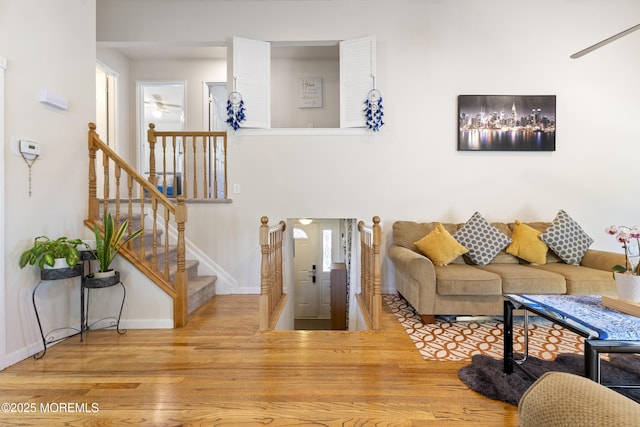 living room with wood finished floors, ceiling fan, baseboards, and stairs