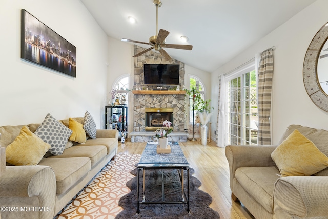 living room with a ceiling fan, wood finished floors, a stone fireplace, and lofted ceiling