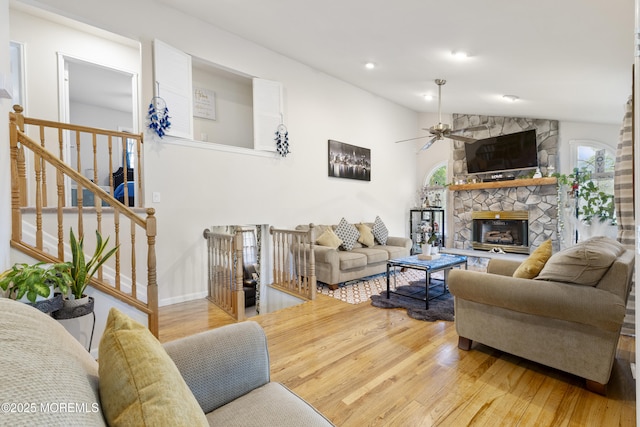 living room featuring a ceiling fan, light wood-style flooring, lofted ceiling, a stone fireplace, and baseboards