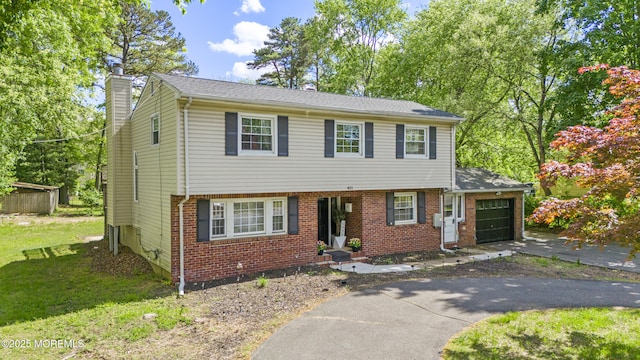 colonial-style house with an attached garage, a chimney, driveway, brick siding, and a front yard