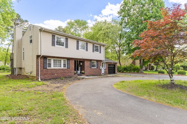 view of front facade with brick siding, driveway, an attached garage, a chimney, and a front yard