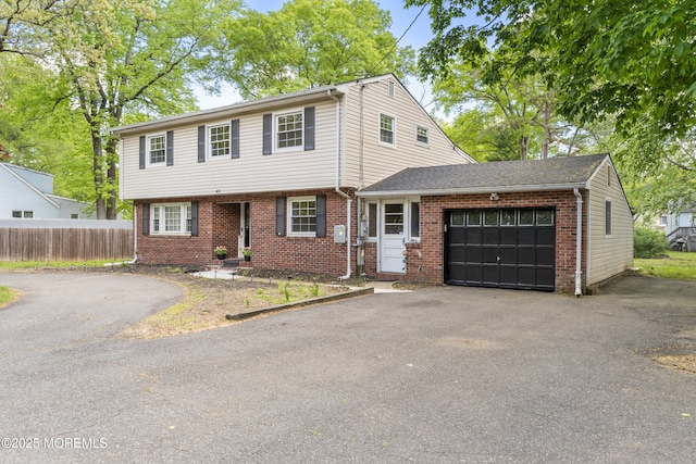 colonial home with an attached garage, brick siding, asphalt driveway, and fence