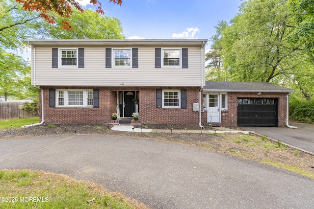 colonial home with driveway, a garage, brick siding, and fence