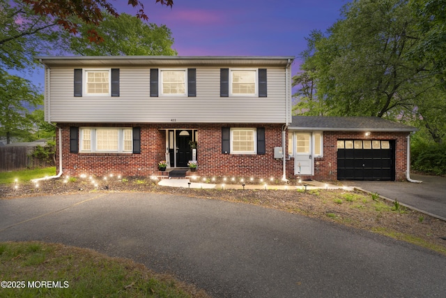 colonial house featuring an attached garage, asphalt driveway, and brick siding