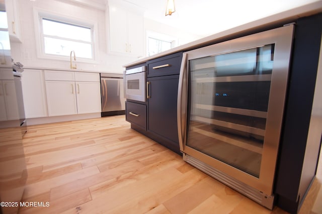 kitchen featuring dishwasher, wine cooler, white cabinetry, a sink, and light wood-style flooring
