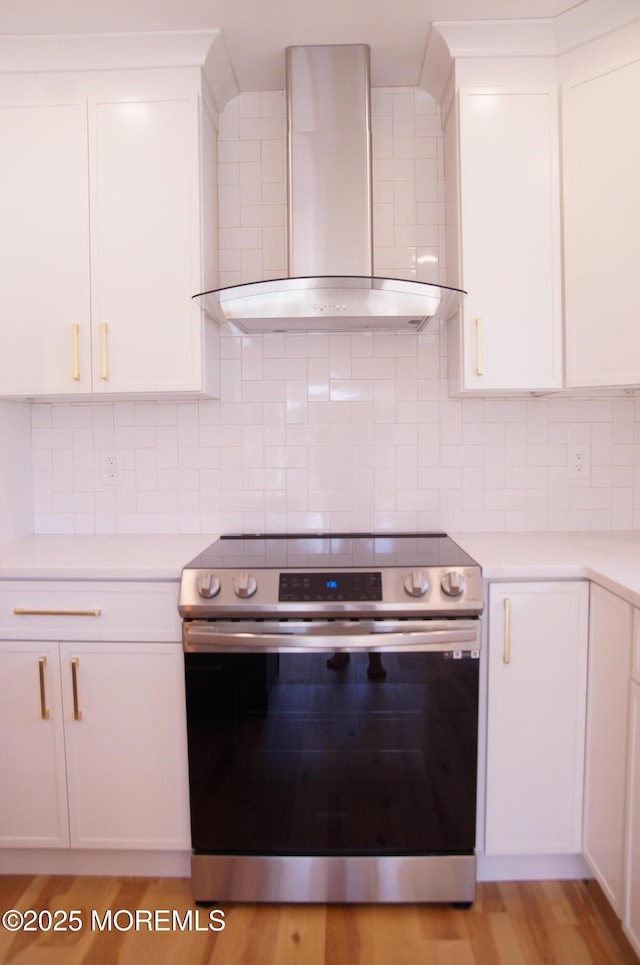 kitchen with wall chimney range hood, electric stove, light countertops, and white cabinets
