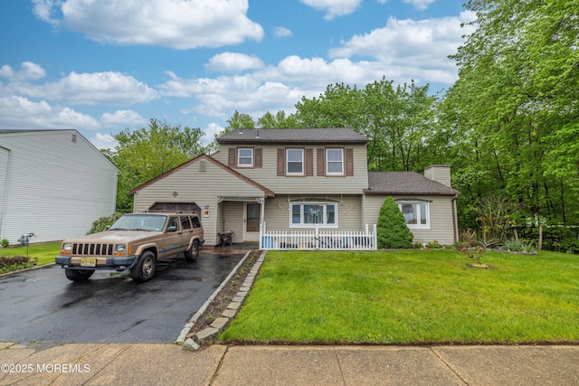 colonial inspired home with asphalt driveway, a chimney, a front lawn, a porch, and a garage